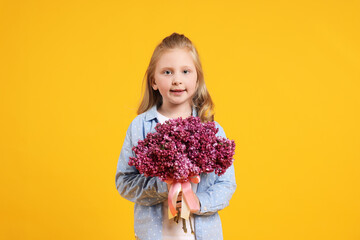 Little girl with bouquet of lilac flowers on yellow background