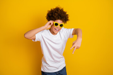 Smiling boy with curly hair in white t-shirt posing against bright yellow background in stylish...