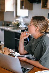  Gen Z woman working from home at cozy kitchen table with laptop and phone. Digital nomad lifestyle, mindfulness, remote work, balance, mental calm and modern freelancing