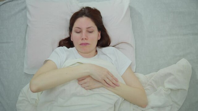 Young adult woman lies in bed in the morning and rubs her hand, who is numb after sleeping in an uncomfortable position