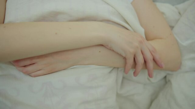 Young adult woman lies in bed in the morning and rubs her hand, who is numb after sleeping in an uncomfortable position