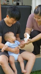 At home, a baby plays with their parents and aunt, sharing moments of laughter and occasional tears. The lively atmosphere reflects the warmth, joy, and emotional ups and downs of family life.
