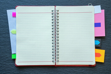 Open spiral bound notebook with colorful bookmarks on black table. Copy space