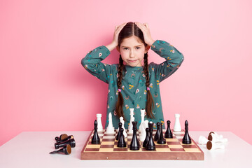 Young girl with braids poses thoughtfully with a chessboard on a pink background expressing playful...