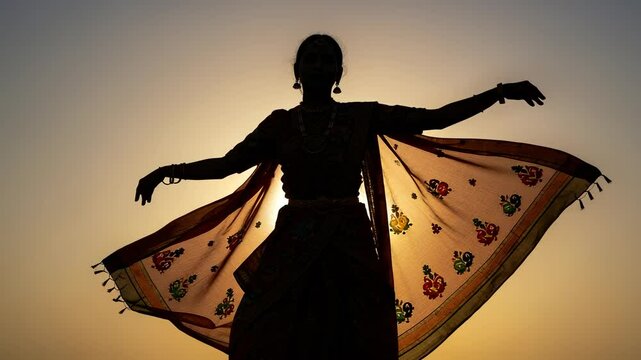 Silhouette of Indian dancer performing traditional dance at sunset with colorful sari