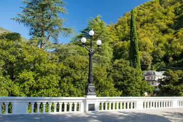 Streets of the southern resort town on the Black Sea coast. White stone railings along the sidewalk of the embankment. A tall lantern with three glass lanterns