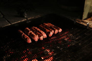Traditional Balkan meat rolls - Cevapi, chevapi - grilling on hot coals over a metal grate. Close view.