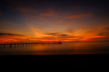 Fiery Sunset over Calm Ocean with Silhouette of Pier