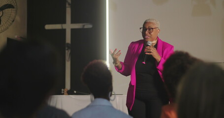 Speaker addressing congregation, holding microphone, delivering powerful sermon in front of a...