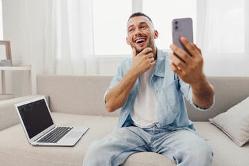 Happy man capturing a selfie in a bright home office, wearing casual clothing and showing joy while using his smartphone. Perfect for lifestyle themes.