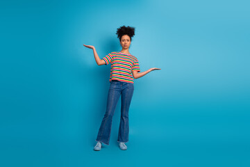 Stylish young woman with afro hairstyle wearing a colorful striped top making a balance gesture...