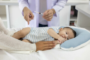 Fototapeta premium A baby is being vaccinated by a doctor, with the mother closely caring for the baby lying on the bed and the doctor holding a syringe. 
