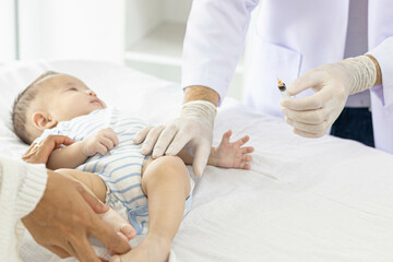 
A baby is being vaccinated by a doctor, with the mother closely caring for the baby lying on the bed and the doctor holding a syringe.
