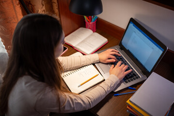 Teen girl doing math homework on computer at desk in the evening. Teenage girl solving math...