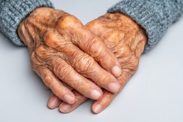 Fototapeta premium Detailed close-up of elderly woman's wrinkled hands, showing the natural signs of aging, and wearing a grey woollen knitted sweater and pale skin tones.