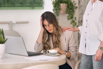 Stressed business woman being consoled by her coworker at the office  by resting a hand on her shoulder.