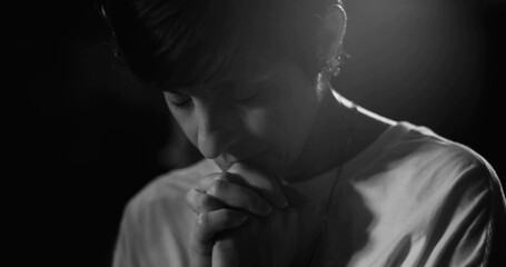 Woman in deep prayer, head bowed and hands clasped, peaceful spiritual reflection, monochrome image capturing faith, hope, and devotion in a moment of quiet contemplation