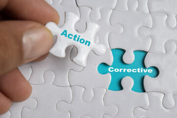 Hand holding piece of jigsaw puzzle with word Corrective action. Business and finance concept