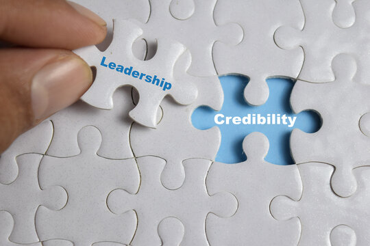 Hand holding piece of jigsaw puzzle with word Credibility and leadership. Business and finance concept