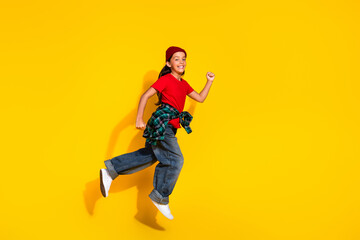 Cheerful girl wearing a red t-shirt and jeans jumping with energy against a vibrant yellow background