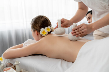 Hot herbal ball spa massage body treatment, masseur gently compresses herb bag on couple customer...