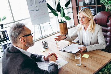 Professional business meeting featuring senior businesswoman and businessman discussing strategies...