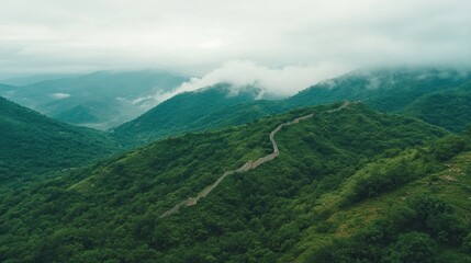 Naklejka premium Curving path of the Great Wall through green mountains with low-hanging clouds brushing the peaks
