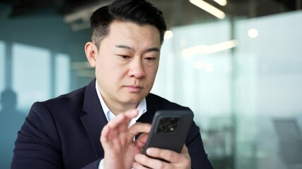 Serious asian businessman is using browsing mobile phone at workplace in business office. Entrepreneur in formal suit is chatting online with client or reading writing message on smartphone. Close up - Powered by Adobe