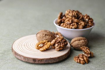 Raw walnuts lying on a wooden board and also peeled kernels in a white bowl on the table close-up