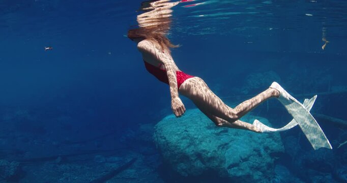 Sexy freediver woman with diving fins swims in transparent blue lake. Underwater view in sunny day
