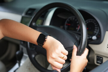 An asian young female driver checks time on watch, online map, stuck in traffic jam and being late for meeting with colleagues, has to delay it. Driving and in rush and stress has to get work in time.