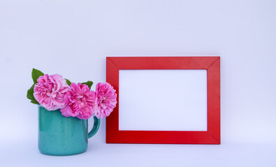 Rose flowers in a mug and red wooden frame with empty space on a white background.