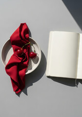 Elegant arrangement of red cherries and cloth on ceramic plate with blank notebook, minimalist style, copy space