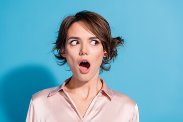 Surprised young woman in pink satin blouse on blue background expressing astonishment with open mouth