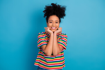 Smiling young woman in a colorful striped shirt posing joyfully against a vibrant blue background...