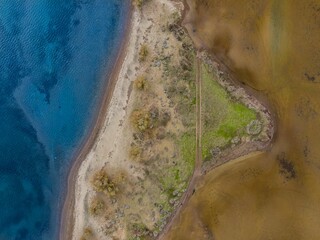 Aerial view of a triangular peninsula with contrasting blue water and earthy tones. © Wirestock