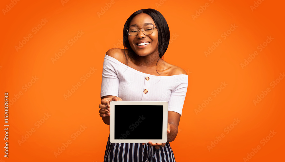 Poster Great Application. Smiling Afro Girl Showing Digital Tablet With Blank Screen Standing In Studio Over Orange Background. Panorama, Mockup