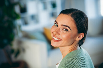 Charming brunette woman smiling cheerfully indoors during a cozy weekend at home in a relaxed and...