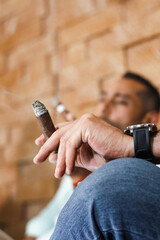 Man holding a lit cigar with another man in the background