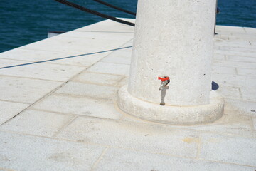 A close up of a white stone pillar with a red spigot on a tiled pier, with the deep blue ocean and...