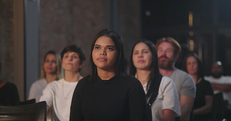 An audience at a church event, with a woman in the foreground listening attentively, others in the...
