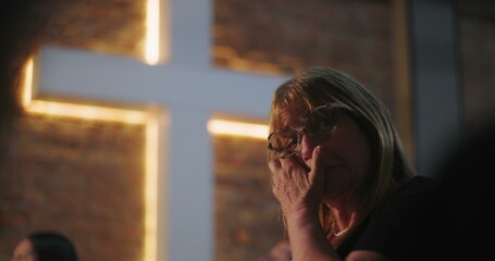 Woman wiping tears, deeply moved, in front of illuminated cross at church, emotional experience...