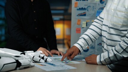 Two business professionals examine financial reports and charts on a table in a modern office, surrounded by colorful sticky notes and a collaborative environment.Noogenesis