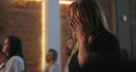Woman wiping tears during prayer in church, deeply emotional moment, illuminated cross, spiritual...