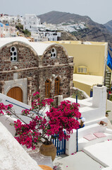 Bright pink bougainvillea blooming beside a stone chapel and whitewashed houses on a sunny terrace in a Greek island village