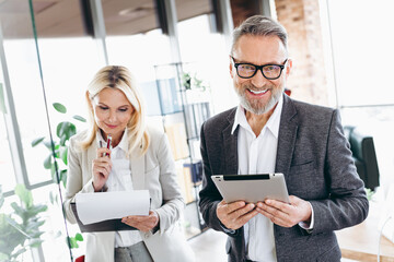 Professional team of mature businesspeople in an office collaborating with technology and documents, showcasing teamwork and dedication