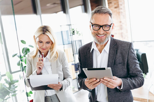 Fototapeta Professional team of mature businesspeople in an office collaborating with technology and documents, showcasing teamwork and dedication