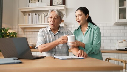Obraz premium Grandmother holding hot coffee cup and encouraging stressful project manager disappointing about deceasing sales or working problem while old man with casual cloth pointing at laptop screen. Myrmidon.