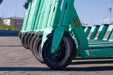 A row of parked green electric kick scooters, vehicles for rent.