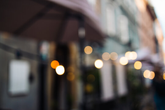 Soft bokeh lights and blurred view of street cafes with umbrellas and hanging bulbs in Warsaw, Poland. A cozy, artistic image ideal for background use, lifestyle visuals, or romantic city atmosphere.
